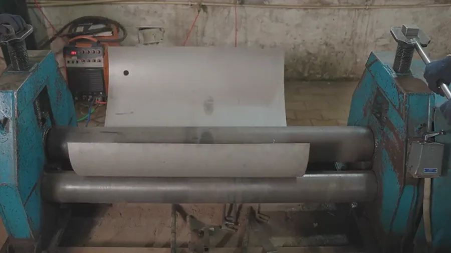 A plate part-way through the rolls, being formed into a vessel shell